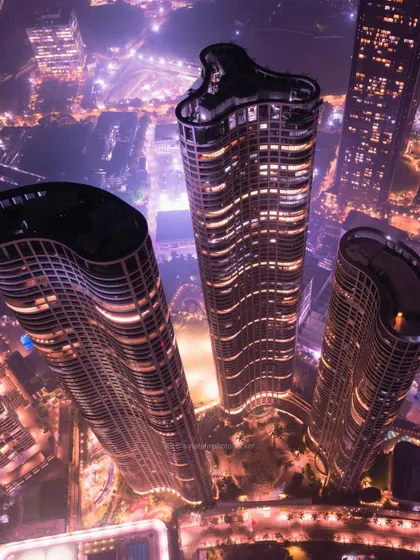 A closer aerial view of the unique, curved architecture of modern skyscrapers in Mumbai, illuminated against the dark city.