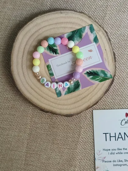 A close-up of the personalized name bracelet for Saina, showing the pretty pastel beads and gold-tone spacers.