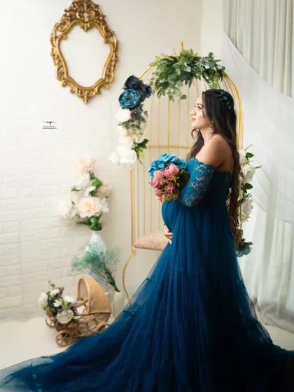 A striking profile shot of the mother-to-be. The elegant teal gown and the floral arrangement on the golden chair create a sophisticated and artistic composition.