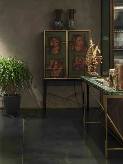 A custom cabinet in the living room displays family portraits, adding a personal and historical layer to the design. The green marble console and golden Garuda sculpture showcase a rich mix of materials and cultural artifacts.