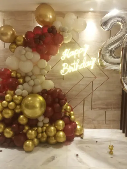 A modern and artistic balloon arrangement for a 20th birthday, using a mix of red, white, and gold balloons against a textured wall.