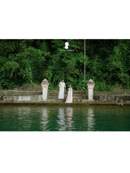 A wider shot of the couple by the temple pond, showing the beautiful green water and surrounding nature.
