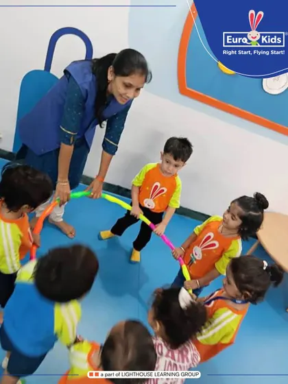 A day dedicated to the world of circles. Here, a teacher guides children in a group activity with hoops, helping them learn about shapes, cooperation, and coordination all at once.