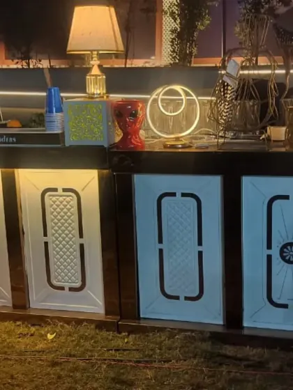 A stylish and modern bar setup for a wedding cocktail party or reception. The bar counter features backlit panels with a geometric design, complemented by contemporary lamps and decor to create a chic and inviting space for guests.