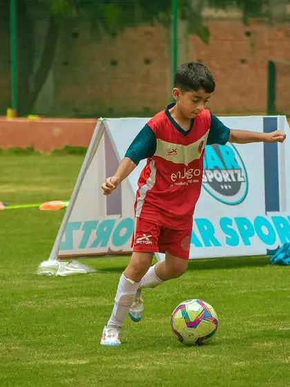 A young player dribbles past the Sar Sportz A-frame banner.