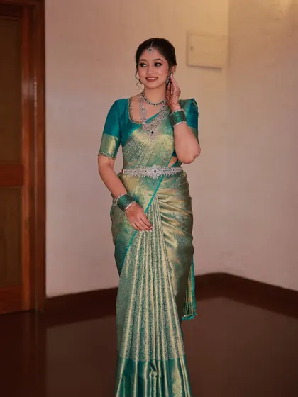 A full-length view of the bride in her teal saree. The makeup and simple, elegant hairstyle create a sophisticated and modern South Indian look.