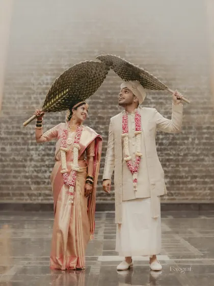 A playful and creative portrait of a South Indian couple. Using traditional hand fans, they create a heart shape above them, smiling at each other.