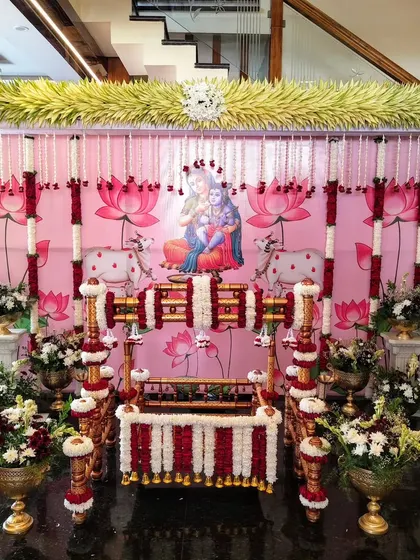 A beautiful naming ceremony setup with a Krishna and Yashoda backdrop and red and white floral decor.