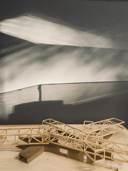 A detailed shot of a balsa wood model of a steel truss system. The shadows cast by the model on the wall are as important as the model itself, revealing its potential to shape light.