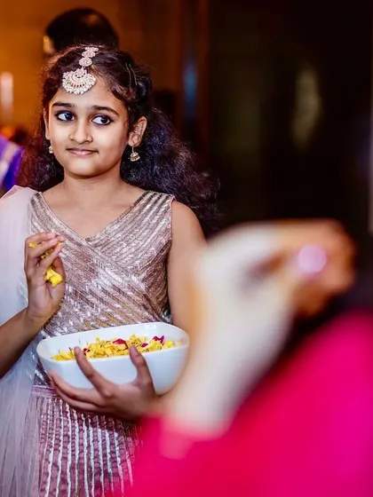 A young flower girl looks on with a shy expression, holding a bowl of petals, a sweet and innocent moment during the bridal entry.