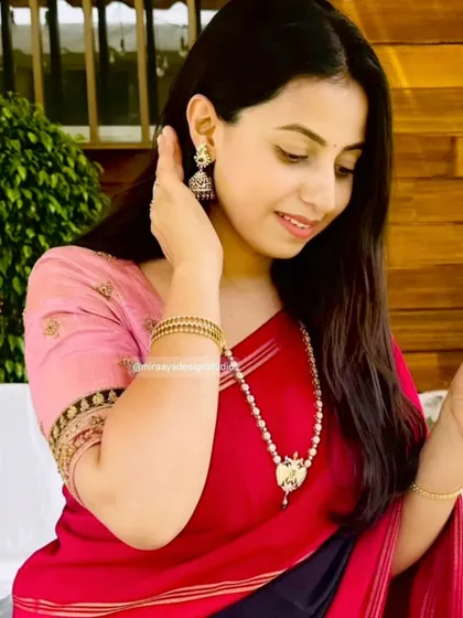 A close-up of Soundarya's look. The simple pink blouse with a detailed sleeve border is the perfect complement to her red and black saree.