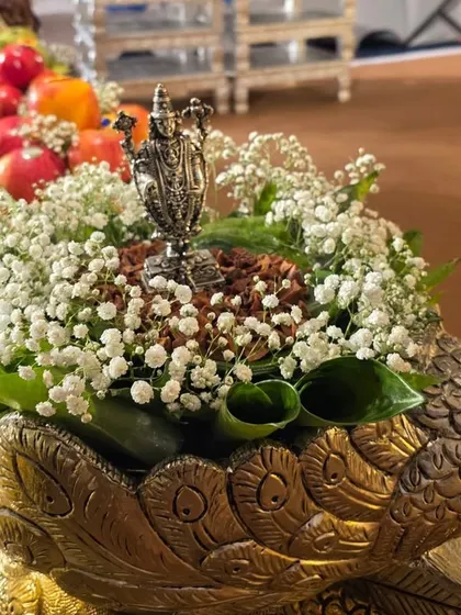 A beautiful offering of betel nuts and leaves with a small silver deity, arranged in a brass peacock bowl with baby's breath.