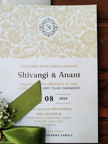 The main invitation card for Shivangi and Anant's Godh Bharai and Tilak ceremony, featuring their custom monogram and a classic floral damask pattern.