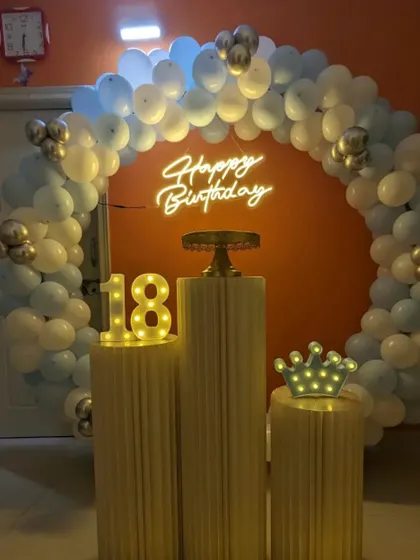 An 18th birthday party with a blue and white balloon arch. The setup includes a marquee number '18' and a light-up crown prop.
