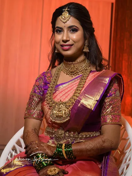 Santhoshi's reception look is a beautiful example of traditional elegance. The rich purple and pink saree is paired with antique gold jewelry and a soft glam makeup look.