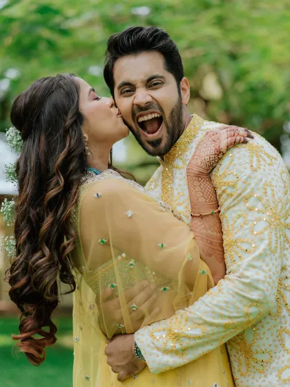 A candid shot of pure happiness. The bride's joyful expression as she gives the groom a kiss on the cheek during their Mehendi is a memory worth saving.