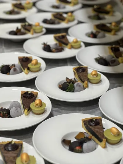 Plated desserts ready for a Christmas event. Each plate features a slice of chocolate tart, a scoop of mochi ice cream, and a pistachio financier.