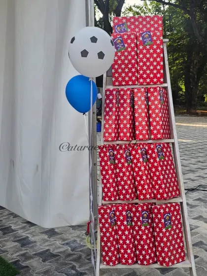 A creative display of party favors at a soccer-themed birthday. The red, star-patterned gift bags are stacked on a white ladder, adding to the event's visual appeal.