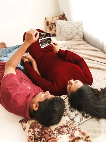 A cozy and intimate lifestyle shot of a couple looking at their ultrasound photo. Lying together on a bed, this captures a quiet, personal moment of bonding with their baby-to-be.
