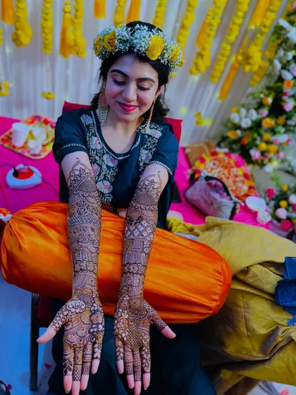 A happy bride posing with her full bridal henna. The vibrant background of her mehndi ceremony makes the photo even more special.