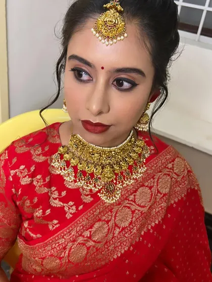 A classic reception look for Dr. Navya. She chose a beautiful red Banarasi saree, which we paired with a bold red lip, winged eyeliner, and an antique gold necklace.