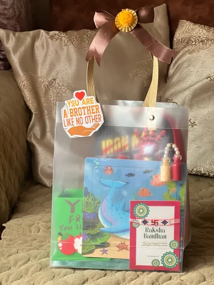 A Rakhi gift hamper in a clear bag, personalized with a "You are a brother like no other" sticker. It includes a Rakhi card and gifts for a young boy.