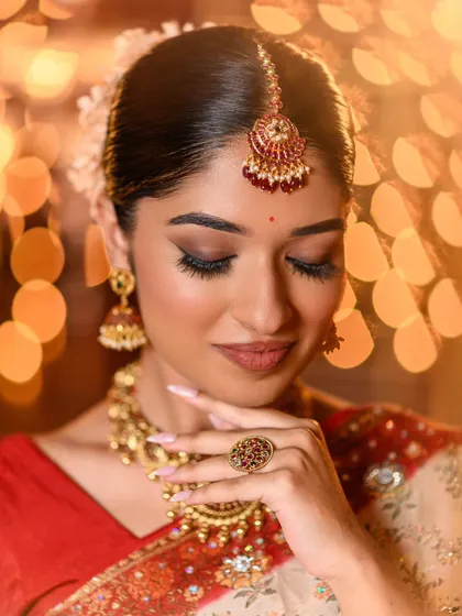 A detailed close-up of the festive eye makeup and traditional maang tikka. The soft focus on the eyes and the perfectly blended skin create a dreamy, celebratory feel.
