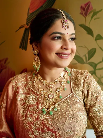 A close-up portrait highlighting the beautiful jewelry and the complementary makeup. The green in the necklace is subtly echoed in her overall warm, peachy tones.
