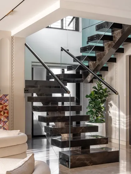 The floating marble staircase is a central feature of the Evelyn duplex. This view from the living area shows how it acts as a sculptural element, connecting the two floors with dramatic flair.