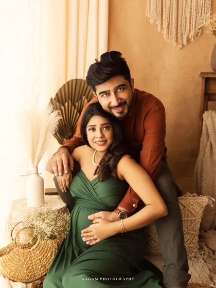 An expecting couple in a cozy, boho-inspired setting. The rich green of her dress and the warm, earthy tones of the studio create a beautiful, natural portrait.