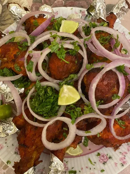 A platter of party-style chicken kababs. The chicken is marinated and cooked until tender, then garnished with fresh onion rings, cilantro, and lime wedges.