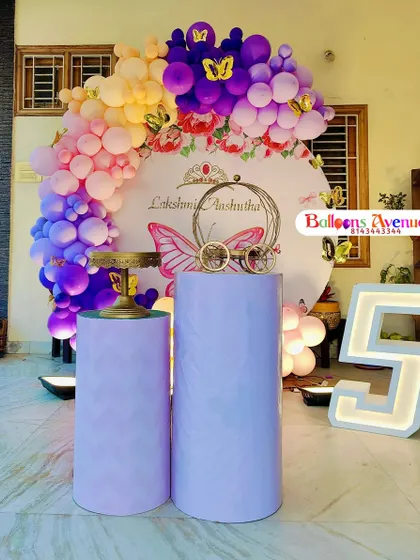A butterfly-themed fifth birthday party with a vibrant purple, pink, and yellow balloon arch over a custom backdrop.