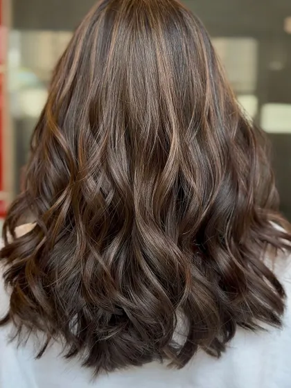 A beautiful example of a chocolate California brunette style. The subtle, warm highlights woven through the dark base create a natural, sun-kissed look, and the soft waves enhance the dimension.