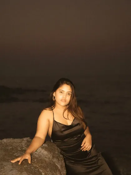 A night portrait on a rocky beach, using a subtle flash to illuminate the subject against the dark ocean. The result is a quiet, intimate, and slightly mysterious image.