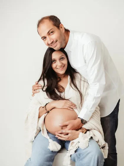 A joyful portrait of the happy couple. The mom-to-be is seated, proudly showing her beautiful bump, while her partner embraces her from behind.