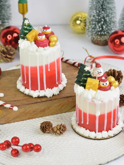 A close-up of my Christmas Cake Candle, featuring a red and white layered design topped with a tiny wax Santa and Christmas tree. It's a cake you can light!