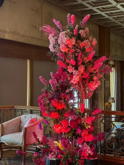 A towering arrangement of pinks and reds adds vertical drama to the Mehendi decor, drawing the eye upward and filling the space with color.