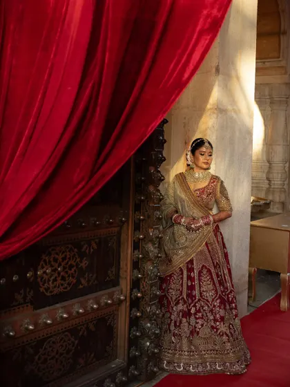 The bride, a vision in her red and gold lehenga, poses against the rich, historic textures of the Chomu Palace. We work with you to ensure your bridal portraits capture the essence of your chosen venue.