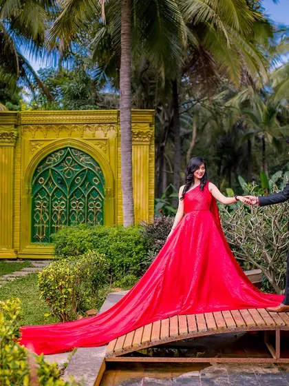 A romantic walk across a bridge in the garden. The long train of the red gown follows the couple, creating a stunning visual line that leads the eye through the photo.