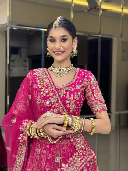 A full shot of the bride in her bright pink lehenga. The overall look is traditional yet modern, with radiant makeup and classic gold jewellery.