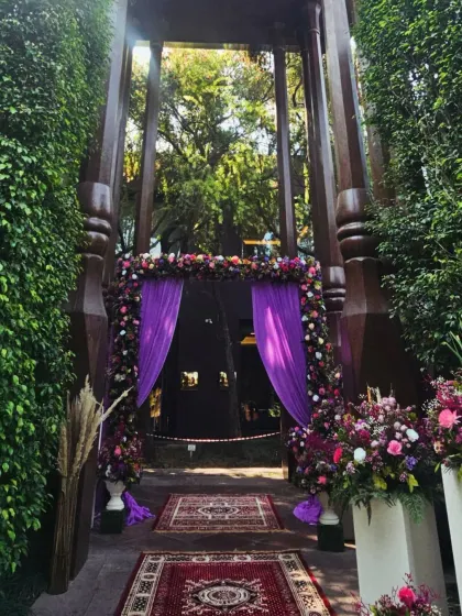 A stunning floral entrance designed with rich purple drapes and a mix of colorful flowers. The traditional rugs on the path add a touch of heritage, creating a warm and regal welcome for guests at The Roseate.