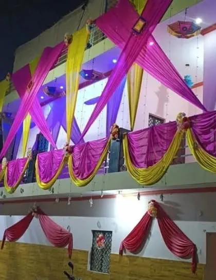 A house facade decorated at night with pink and yellow drapes in a criss-cross pattern, illuminated by blue and purple lights.