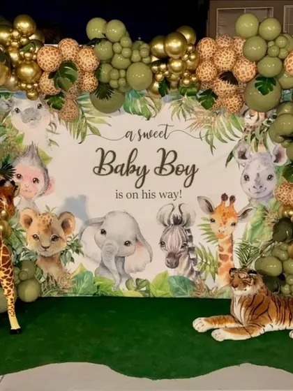 A jungle-themed baby shower backdrop announcing "a sweet Baby Boy is on his way," framed by a lush balloon garland and accompanied by plush animal props.