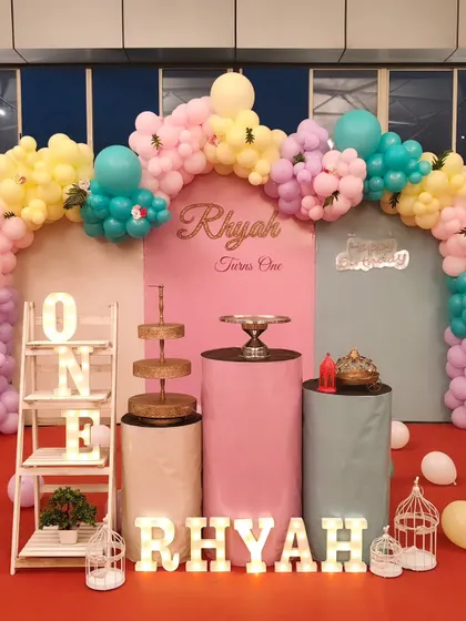 A soft and dreamy pastel theme for a first birthday. The decor features a gentle balloon arch, multiple cake stands at different heights, and light-up 'ONE' and name signs for a clean and modern look.