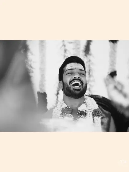 A joyful black and white close-up of the groom laughing heartily during the ceremony.