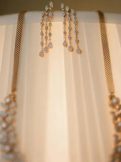 An artistic shot of bridal jewelry, with earrings and a necklace elegantly draped over a lampshade.
