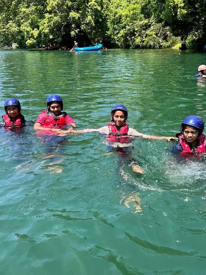 Four girls hold hands and float in the clear green water of the Kali River, enjoying a swim break during their camp.