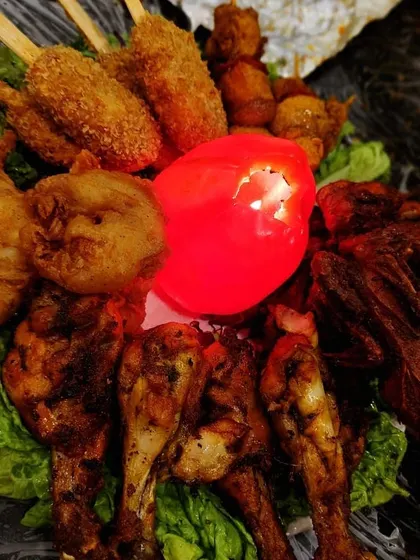 A vibrant platter of assorted non-veg starters, including chicken drumsticks, fried quail, and crispy prawns, arranged on a bed of lettuce. The glowing centerpiece adds a festive touch.