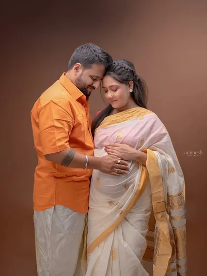 A traditional maternity photoshoot featuring a couple in classic Indian attire. The wife wears a beautiful white and gold saree, creating a timeless and culturally rich portrait.
