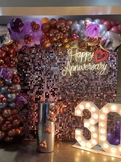 A glamorous 30th-anniversary party with a rose gold shimmer wall, a balloon arch, and large '30' marquee numbers.